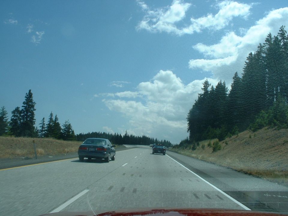 Cars on a highway with trees and clouds