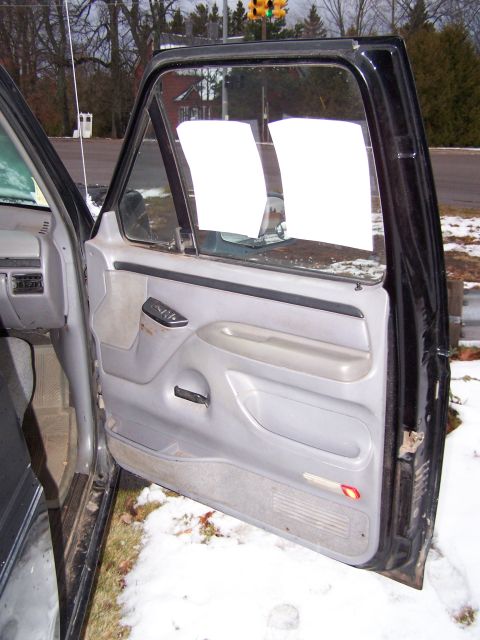 1996 Ford Bronco - View of the interior door panel and window of a vehicle, with white paper obscuring the view outside.