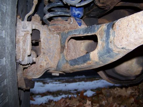 1996 Ford Bronco - Close-up view of heavily rusted vehicle suspension components, showing a coil spring and part of a tire.