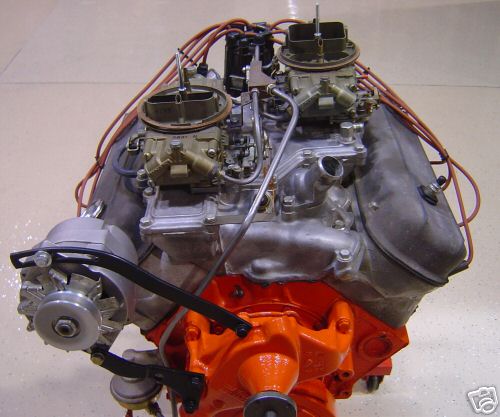 Orange V8 engine block with dual carburetors, distributor, and alternator. The engine is viewed from the front-right