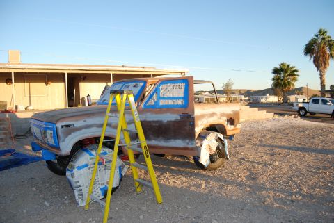 1982 Ford Bronco - Ford Bronco being prepped for paint, with a ladder and masking tape visible. Another truck is in the background.