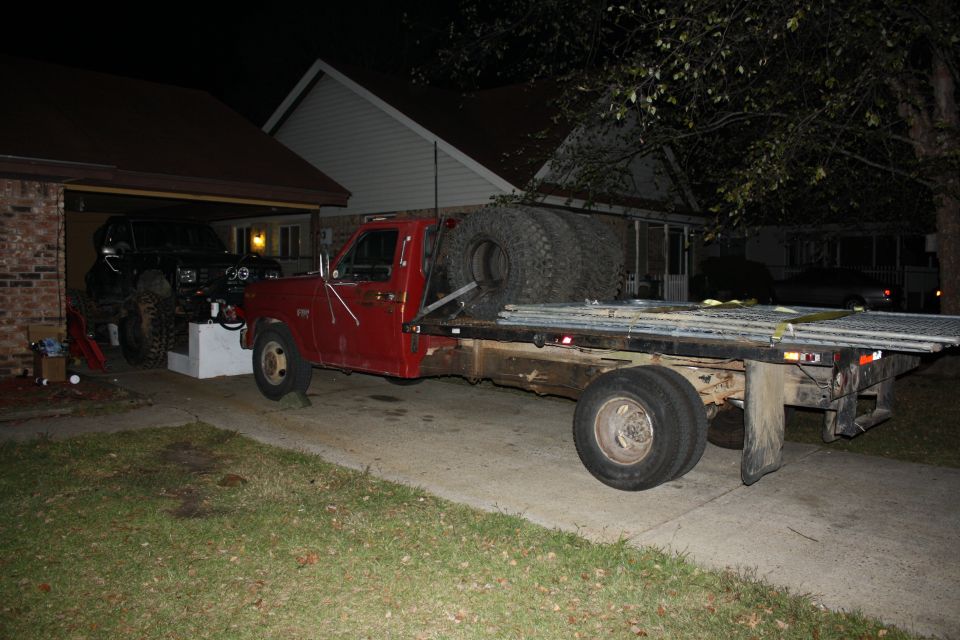 Red flatbed truck carrying large tires, with a black SUV parked nearby