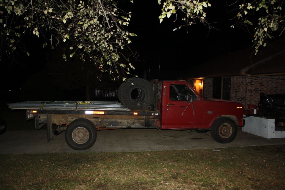 Red flatbed truck with a spare tire mounted on the side of the bed, carrying metal poles