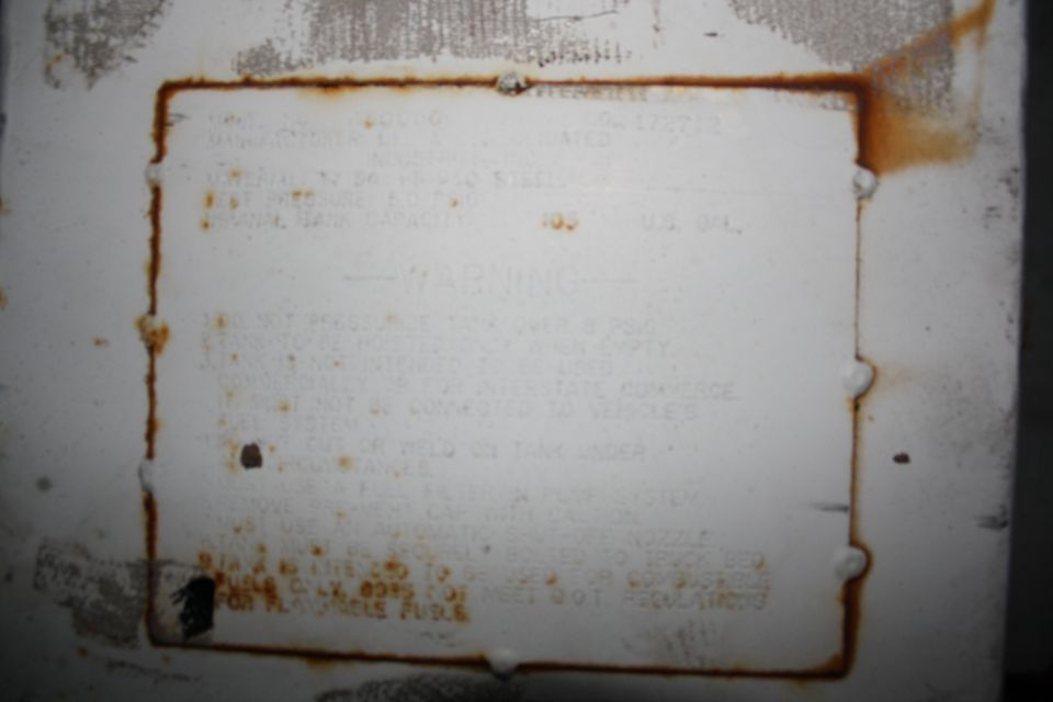 White vehicle identification plate with rust stains and some readable text