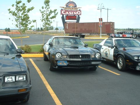 1999 Ford Crown Victoria - A black 1978 Chevrolet Camaro is parked in front of a casino, with a police car to its right.