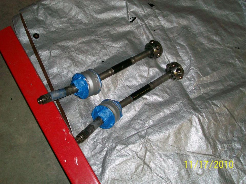 two drive axles with blue tape on the boots, resting on a tarp next to a red object