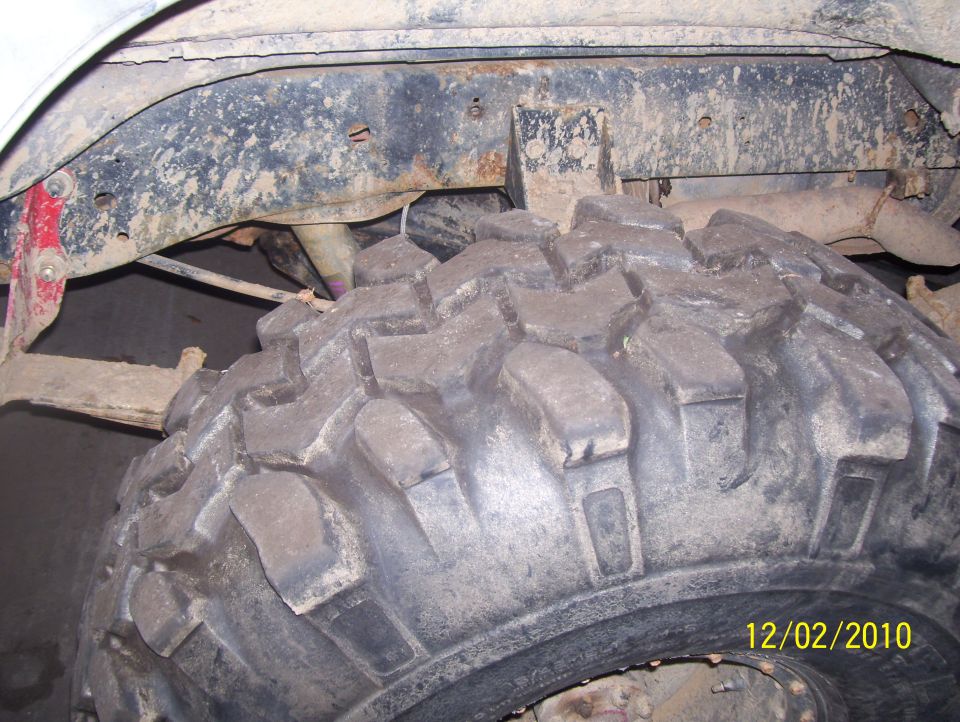 Close-up of a large off-road tire and dirty suspension parts, with a date stamp '12/02/2010' and 'SUPERMOTORS' logo