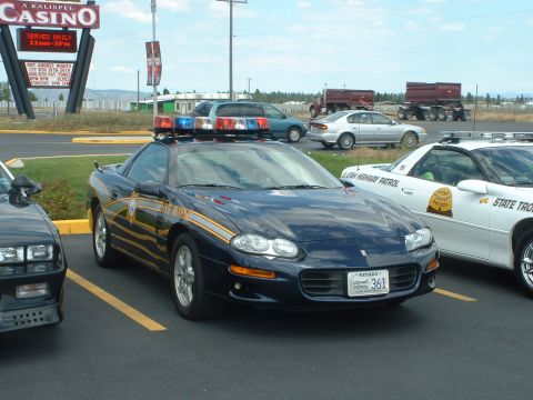 1999 Ford Crown Victoria - A dark blue police car with a light bar is parked in a lot next to a white state trooper vehicle.