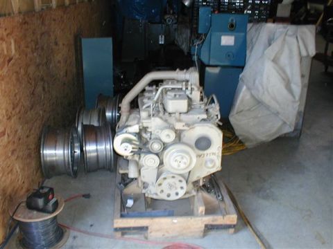 1986 Jeep Wagoneer - An engine sits on a wooden pallet, with several large metal wheels stacked to its left. Other equipment is visible in the background.