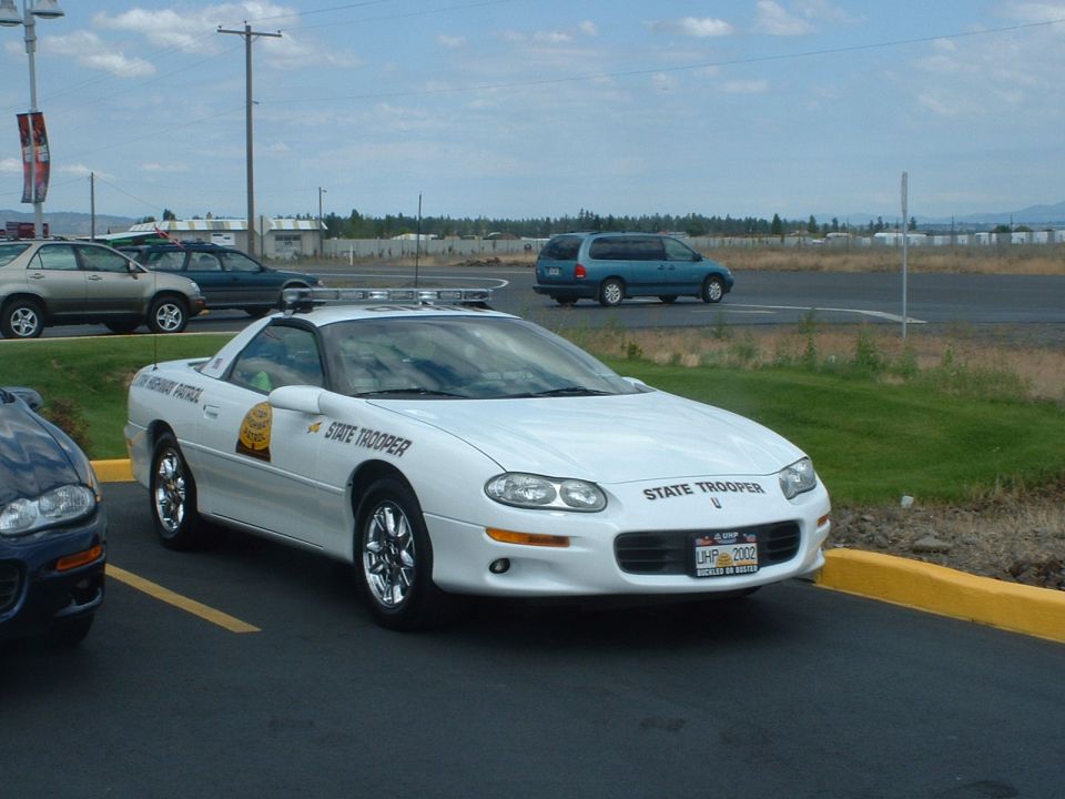 White Chevrolet Camaro police car with "State Trooper" text, parked in a lot