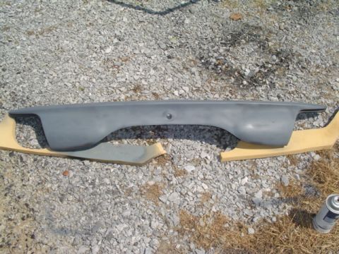 1999 Ford Taurus - A gray car part is laid out on gravel, with a can of spray paint nearby, suggesting preparation for painting.