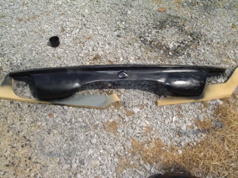 1999 Ford Taurus - A car part, possibly a bumper or trim piece, is laid out on a gravel surface with some tan protective material.