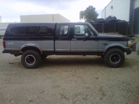 1994 Ford F-150 - This two-tone pickup truck, a 1994 Ford F-150, is equipped with a black camper shell for added utility.