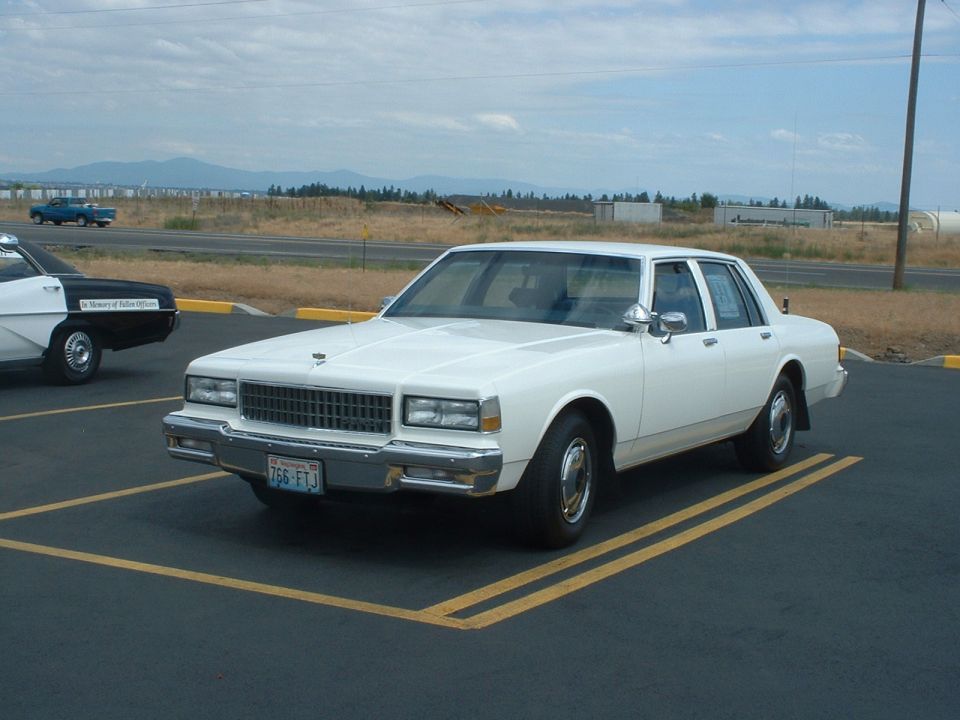 White sedan parked in a parking lot, front quarter view. License plate reads 766 FTJ