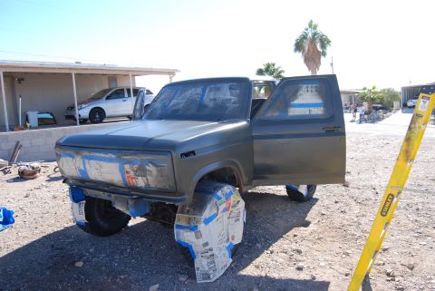 1982 Ford Bronco - A dark green Ford Bronco is prepped for painting with its wheels covered in newspaper.