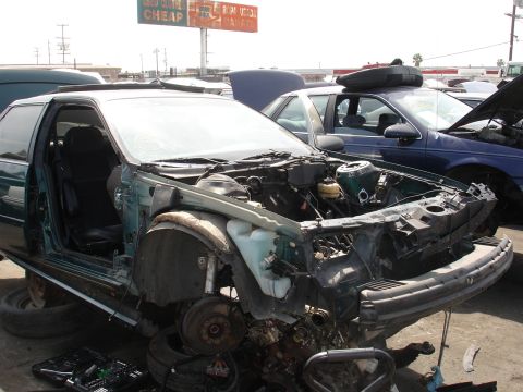 1993 Ford Taurus - Junkyard scene with a damaged 1993 Ford Taurus coupe in the foreground.