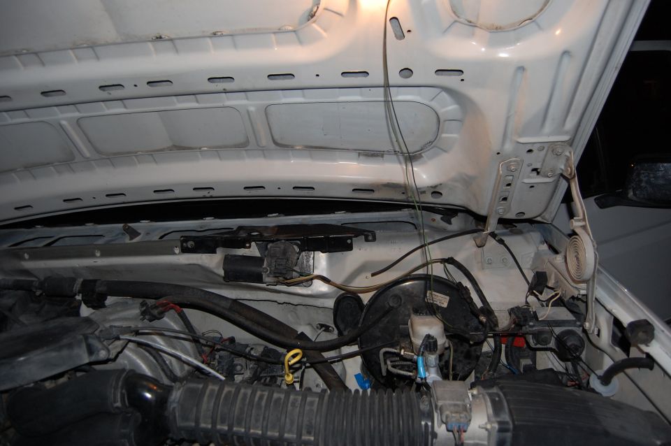 White vehicle engine bay with open hood, showing hoses, wires, and brake booster