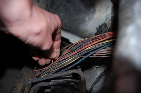 1994 Ford Bronco - Close-up of a hand inspecting a damaged vehicle wiring harness.