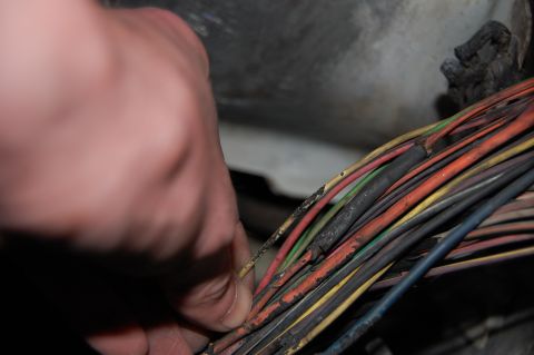 1994 Ford Bronco - A close-up shows a hand inspecting a bundle of damaged and frayed electrical wires within a vehicle.