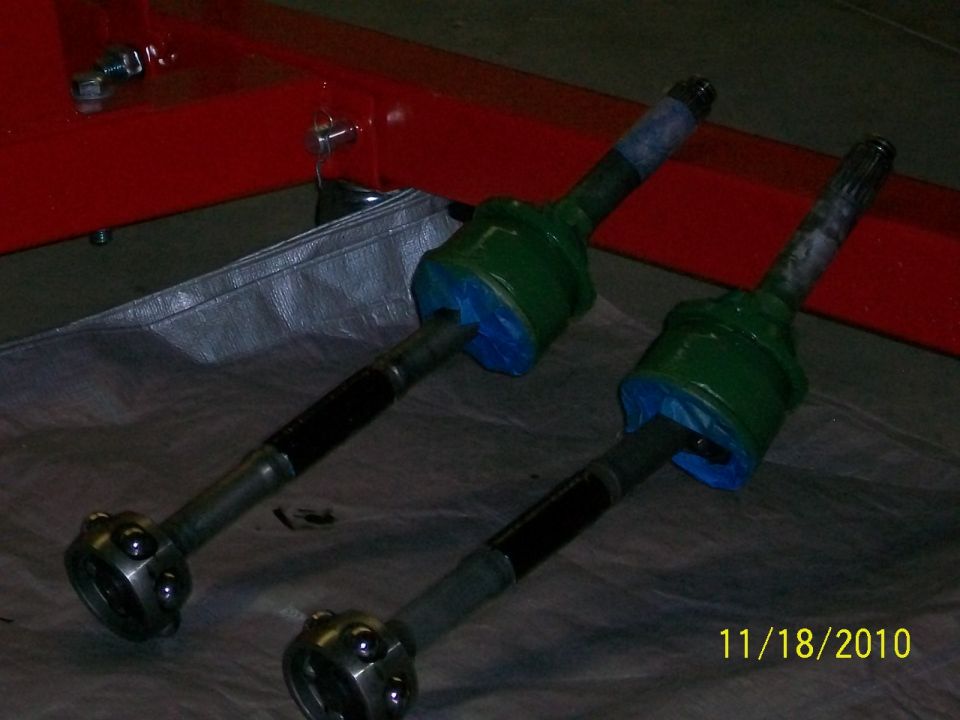 Two green CV axles with blue protective covers on a gray tarp