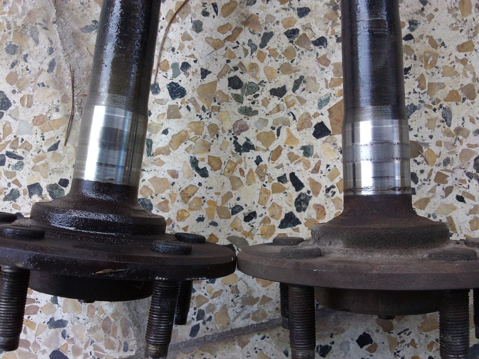 Two metal axle shafts with hub flanges on terrazzo floor
