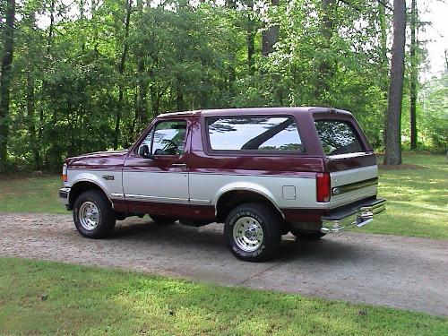 Two-tone maroon and silver full-size Ford Bronco parked among trees