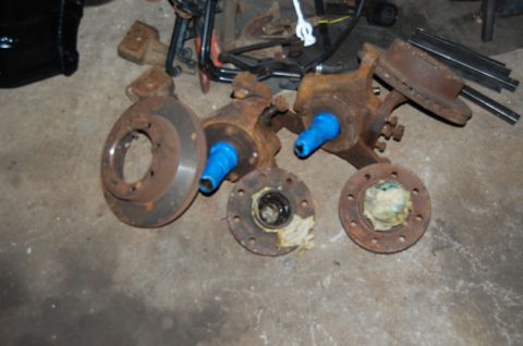 1994 Ford Bronco - Several rusted vehicle axle parts, including brake rotors and hubs, are laid out on a concrete floor.