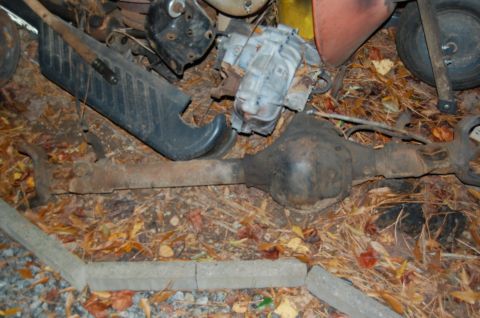 1994 Ford Bronco - A rusty axle assembly and other vehicle parts are lying on the ground covered in leaves.