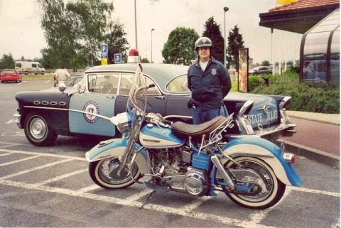 1991 Ford Crown Victoria - A police officer stands between a vintage Buick Century police car and a motorcycle.