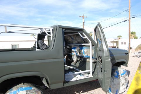 1982 Ford Bronco - This gray SUV is undergoing a paint job, with its interior protected by a roll cage and taped wheels.