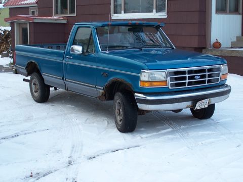 1994 Ford F-150 - A blue Ford F-150 pickup truck is parked in a snowy driveway with a house in the background.
