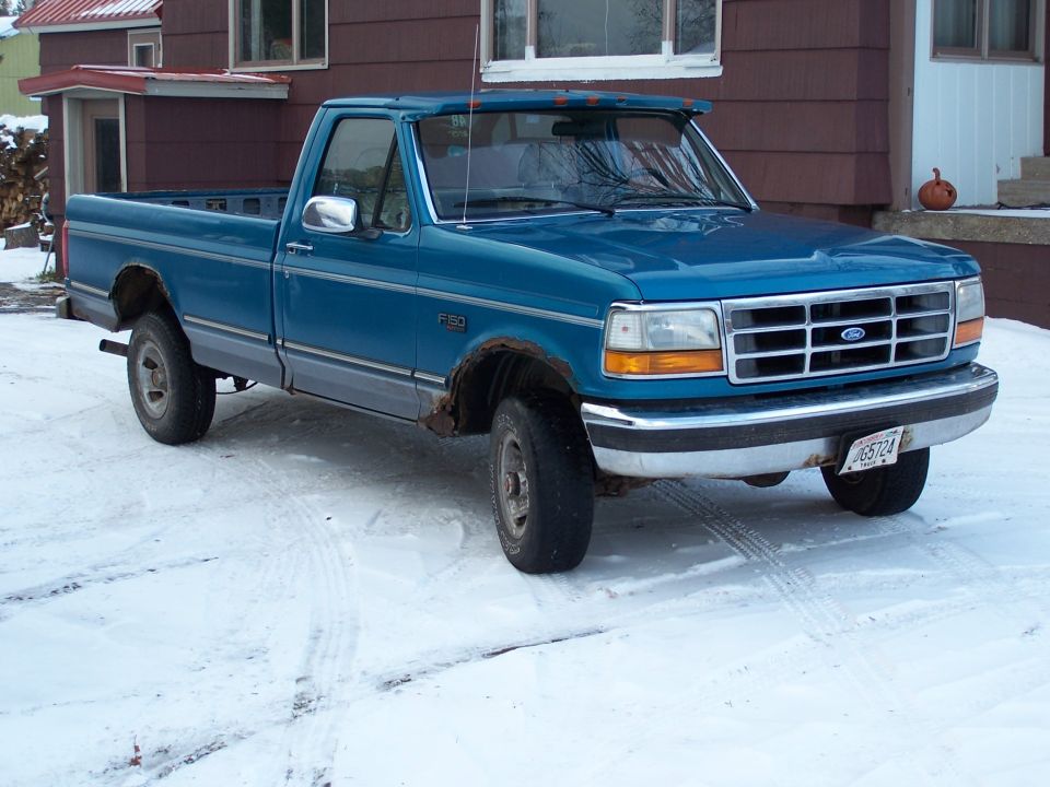 Blue Ford F-150 pickup truck with rust on wheel wells, parked in snow
