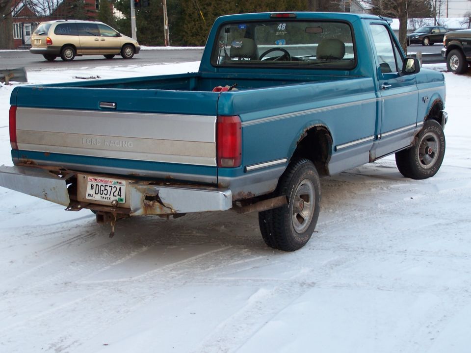 Rear view of a blue 1994 Ford F-150 pickup truck with a dented bumper and a Wisconsin license plate