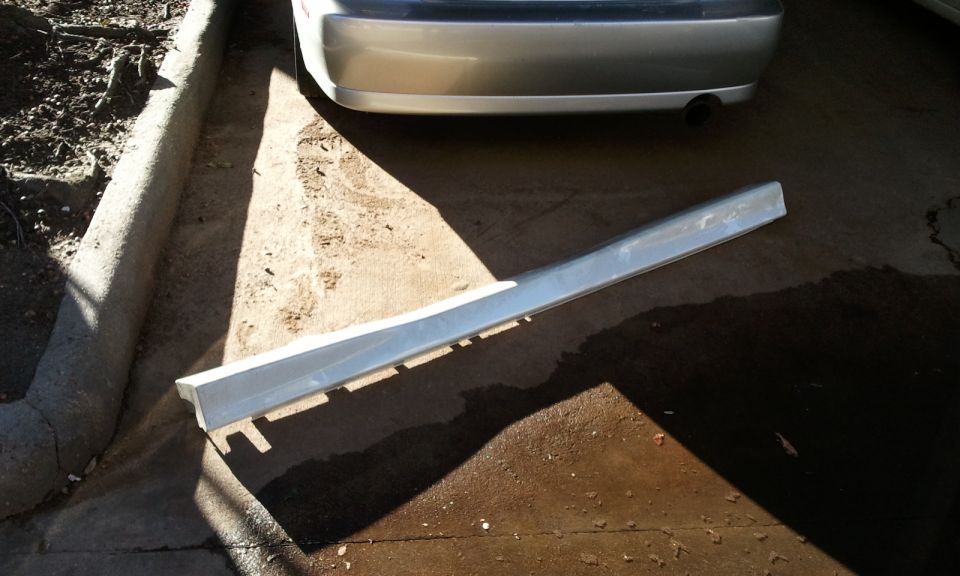 Silver car side trim piece lying on concrete next to a car bumper