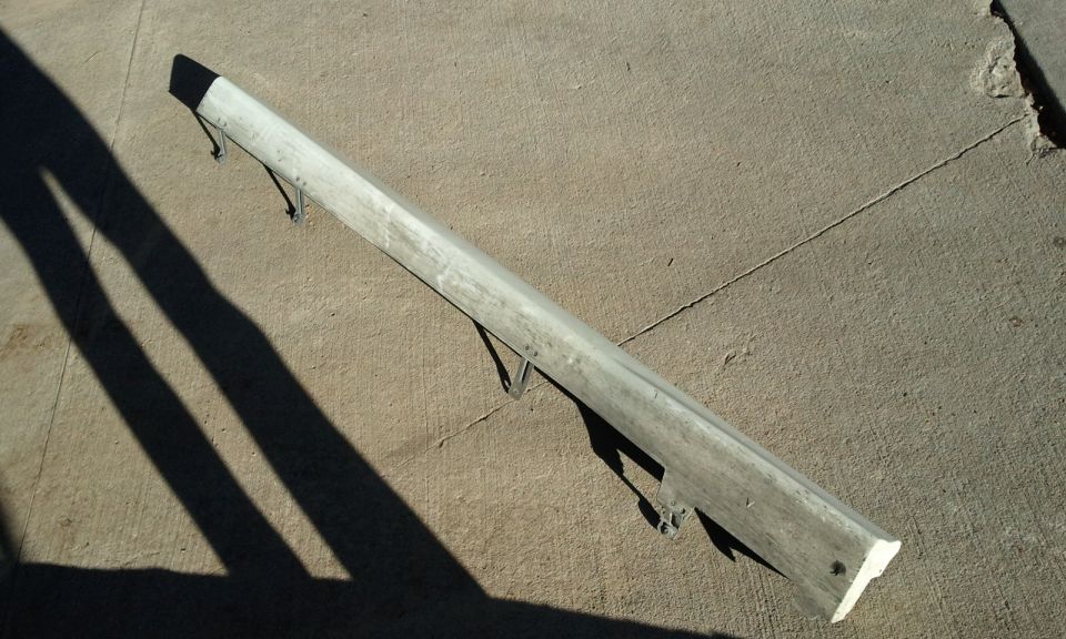 Silver car bumper with mounting brackets, lying on concrete
