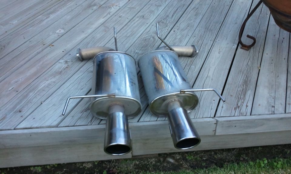 Two chrome exhaust mufflers with bent hangers on a wooden deck