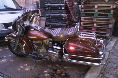 1991 Ford Crown Victoria - A brown motorcycle is parked outdoors, with a partial view of a car and stacked pallets in the background.