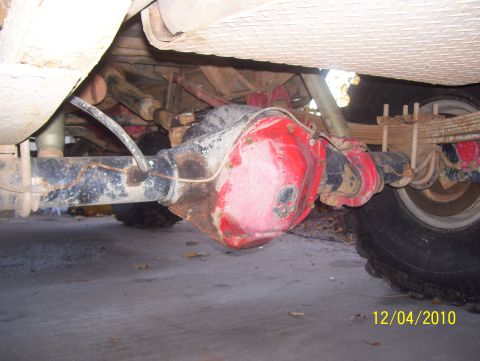 1978 Ford Bronco - Close-up view of a red rear axle assembly, leaf springs, and a tire, likely from an older vehicle.