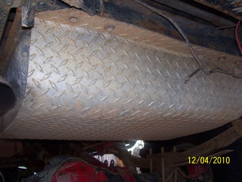 1978 Ford Bronco - Close-up view of a diamond plate fuel tank and suspension components on the underside of a vehicle.
