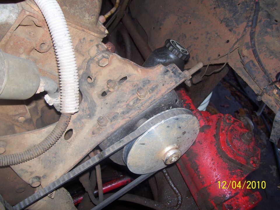 Close-up of a vehicle's engine pulley and belt system, with a black reservoir cap