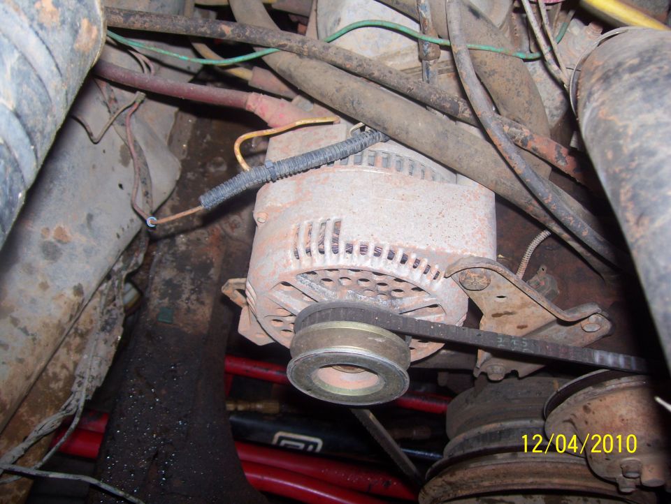 Close-up of an alternator with a belt, surrounded by engine hoses and wires