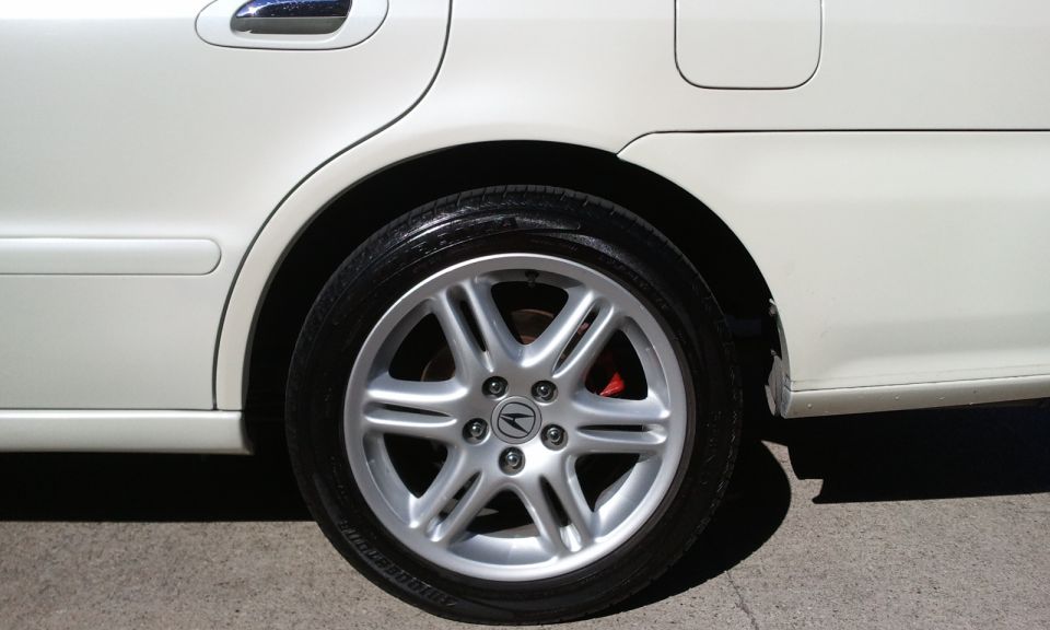 Silver 7-spoke Acura alloy wheel with red caliper on a white sedan