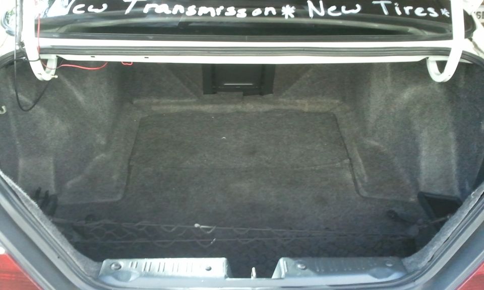Open empty carpeted trunk of a sedan with handwritten 'New Transmission New Tires' text on lid.