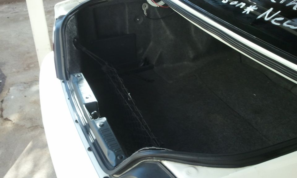 Open trunk of white sedan with black carpet and mesh cargo net