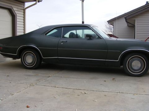1971 Mercury Cyclone - A dark coupe with a distinctive body style is parked on a concrete driveway next to a garage.