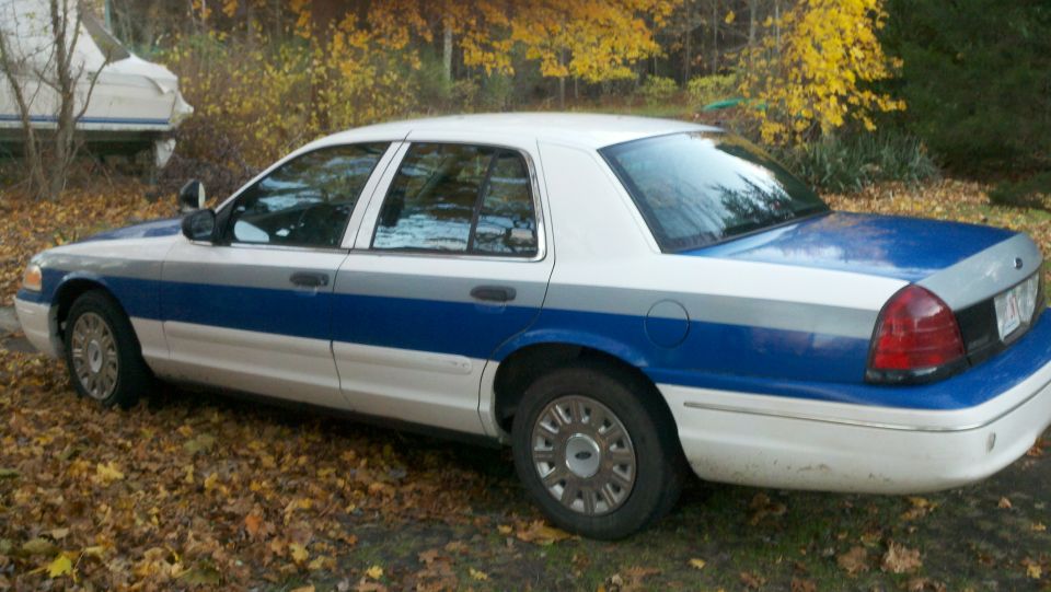 White and blue Ford Crown Victoria parked on a leaf-covered ground