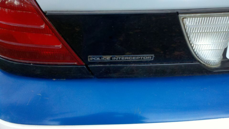 Rear of a 2003 Ford Crown Victoria Police Interceptor with a blue bumper and a black trim panel with 'POLICE INTERCEPTOR' text
