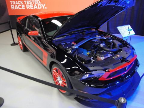 1993 Ford Taurus - Black Ford Mustang with red racing stripes and wheels is displayed with its hood open at an auto show.