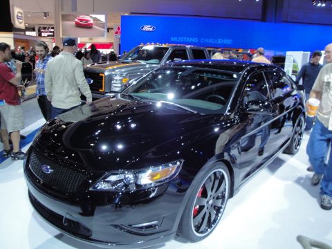 1993 Ford Taurus - A black Ford sedan is displayed at an auto show, with a Ford truck visible behind it.