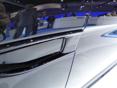 1993 Ford Taurus - Close-up of chrome trim on a white vehicle, with reflections of attendees and displays visible.
